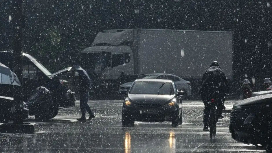 Moody urban street scene in heavy rain with cars and pedestrians.